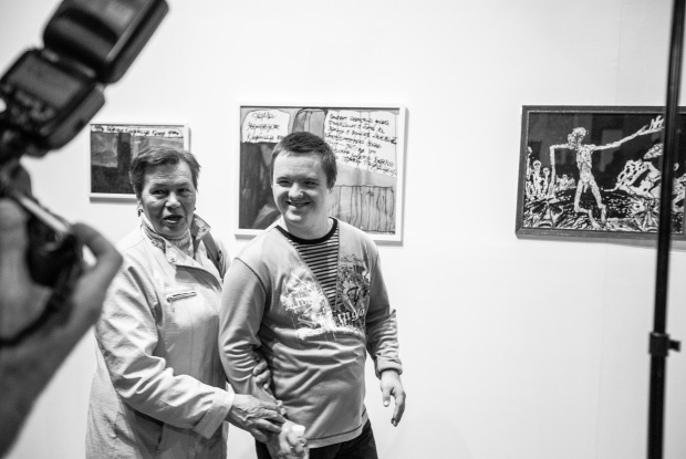 Schwarz-weiß-Foto von Zhenya Holubentsev vor seinen Bildern in einer Ausstellung in Kiew.