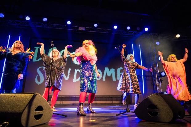 Vier Drag Queens mit Down-Syndrom in prächtigen, bunten Kostümen auf der Bühne